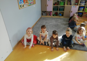 Dziewczynki siedzą na brzegu dywanu i uderzają dłońmi w podłogę.