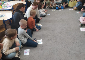 Dzieci siedzą wspólnie na dywanie z rodzicami i układają świąteczne puzzle.