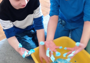 Dwóch chłopców dotyka dłońmi piankę do golenia wymieszaną z niebieską w farbą.