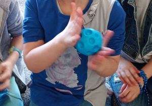 Dziewczynka w niebieskiej bluzce masuje dłonie piłeczką z wgłębieniami.