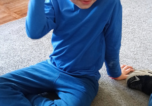 Chłopiec ubrany na niebiesko bawi się niebieskimi piórkami.
