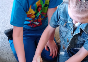 Dwójka dzieci: chłopiec i dziewczynka próbują złapać niebieskie pomponiki szpatułkami.