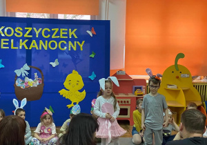 Dwoje dzieci w stroju zajączka stoją i recytują wierszyki, reszta dzieci siedzi z tyłu na dywanie.
