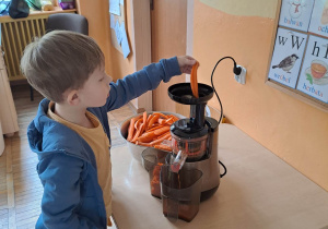Chłopiec stoi i wkłada do wyciskarki marchewkę.