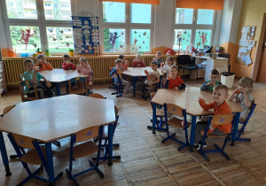 Dzieci siedzą przy stolikach i trzymają w rękach sok z marchewki.