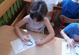 Dziewczynka i chłopiec w niebieskich bluzeczkach przy stoliku malują niebieską farbą motyle