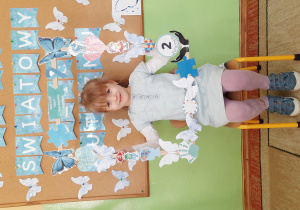Dziewczynka w niebieskiej sukience pozuje do zdjęcia w fotobudce z symbolami dotyczącymi autyzmu