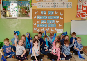Dzieci na dywanie pozują do zdjęcia machając niebieskimi wstążkami