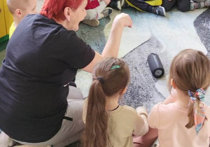 Pani Basia siedzi z dziećmi na dywanie pokazując ruchy to piosenki