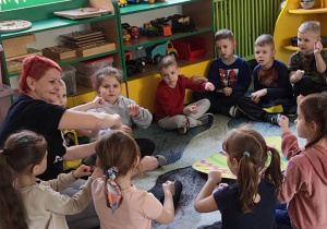 Pani Basia siedzi z dziećmi w kole na dywanie, po środku koła leży tekturowe jajko.