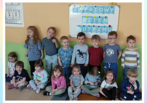 Zdjęcie grupowe dzieci w sali przedszkolnej na tle napisu Światowy Dzień Autyzmu.