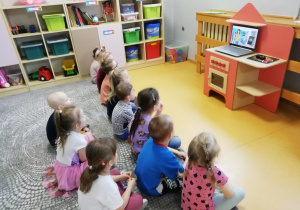 Przedszkolaki siedzą na dywanie i oglądaj na laptopie film „Jak możemy dbać o Ziemię?”.