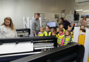 Dzieci stoją obok maszyny wycinającej wydrukowane naklejki.