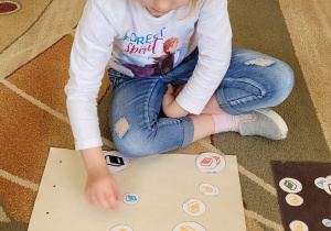 Dziewczynka siedzi na dywanie i segreguje emblematy książek według kolorów