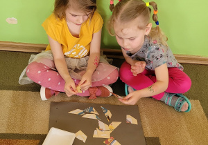 Dwie dziewczynki siedzą na dywanie i układają obrazek przedstawiający zasadę korzystania z książek