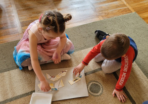 Dziewczynka i chłopiec siedzą na dywanie i układają obrazek przedstawiający zasadę korzystania z książek