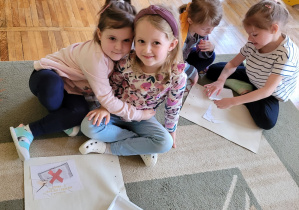 Dwie dziewczynki siedzą na dywanie i prezentują ułożony obrazek, a kolejne dwie dziewczynki układają obrazek