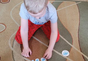 Chłopiec siedzi na dywanie i układa emblematy książek od najmniejszego do największego