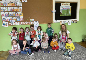 Szczęśliwe przedszkolaki pozują do zdjęcia z Panią Pleciugą i w rączkach trzymają wykonane przez siebie króliczki.