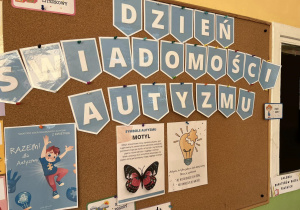 Zdjęcie przedstawia dekorację tematyczną z okazji Dnia Świadomości Autyzmu. Na tablicy wisi napis oraz plansze związane z tym dniem