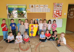 Przedszkolaki z grupy „Stokrotki” stoją i siedzą na dywanie i trzymają projekt lalki w dłoniach.