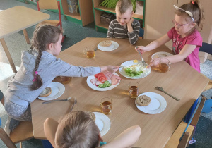 Dzieci siedzące przy stoliku nakładają przygotowane produkty na swoje kanapki
