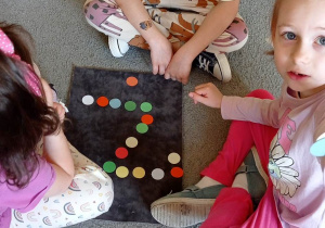 Troje dzieci pozuje do zdjęcia z ułożoną literą „Ż” z kolorowych kółeczek.