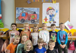 Dzieci z grupy Motylki pozują do zdjęcia na tle kolorowanek XXL strażaka i wozu strażackiego.