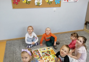 Dzieci siedzą w kole, pośrodku nich leży ilustracja związana z pszczołami.