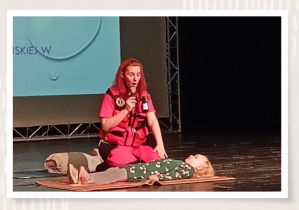 Zdjęcie przedstawiające Panią ratownik na scenie podczas pokazu pierwszej pomocy.