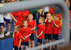 Uczestnicy czekający na swoją kolej w zawodach. Zdjęcie przedstawia stojące dzieci w czerwonych koszulkach z biedronką.