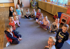 Dzieci wraz z Panią Kasią siedzą na dywanie i pokazują języki.