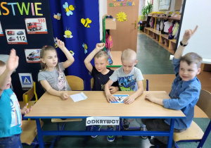 Dzieci z grupy Odkrywców podnoszą rękę do góry na znak, iż ułożyły puzzle przedstawiające znak drogowy.