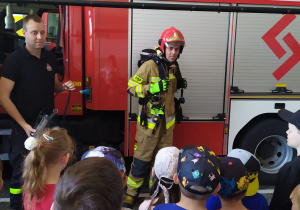 Dzieci oglądają strażaka, który prezentuje strażacki strój.