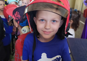 Chłopiec pozuje do zdjęcia w hełmie strażackim.