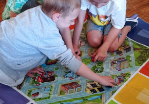 . Troje chłopców bawi się samochodzikami na macie przedstawiającej miasto.