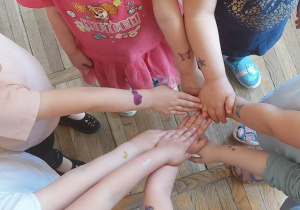 Dzieci w kółeczku pokazują sobie rączki z wykonanymi tatuażami brokatowymi.