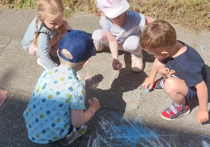 Dzieci malują kredą kolorowe rysunki na chodniku.