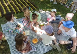 Dzieci z grupy Smerfy świętują swoje święto na pikniku częstując się smakołykami.