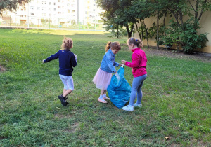 Trzy dziewczynki wrzucają śmieci do niebieskiego worka.