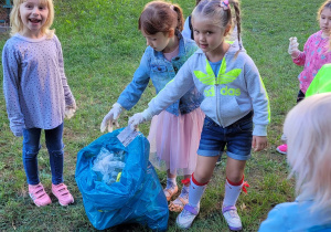 Dziewczynki z grupy motylki wrzucają zebrane śmieci do worka.