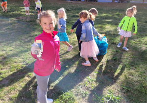 Dziewczynka pokazuje zebrane śmieci, a pozostałe dzieci je zbierają.