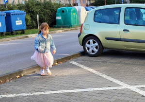 Dziewczynka w różowej sukience zbiera śmieci na parkingu.