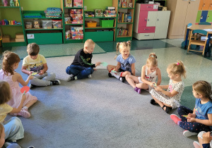 Dzieci siedzą na dywanie i przekazują sobie kółka za pomocą klamerek.