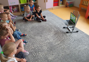 Dzieci siedzą na dywanie oglądając z laptopa film edukacyjny o sprzątaniu świata.