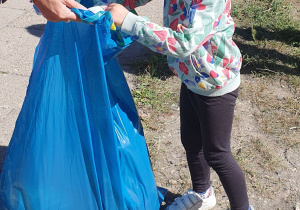 Dziewczynka wrzuca zebrane śmieci do niebieskiego worka.