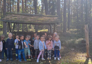 Dzieci stoją przy paśniku w lesie i pozują do zdjęcia.