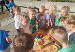 Dzieci stoją przy stoliczku i częstują się smakołykami przygotowanymi specjalnie z okazji ich święta.