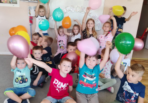 Dzieci z grupy Tropiciele pozują z balonami na tle napisu Dzień Przedszkolaka.