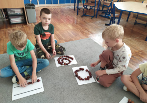 Dzieci układają z kasztanów na kartkach różne wzory i szlaczki.